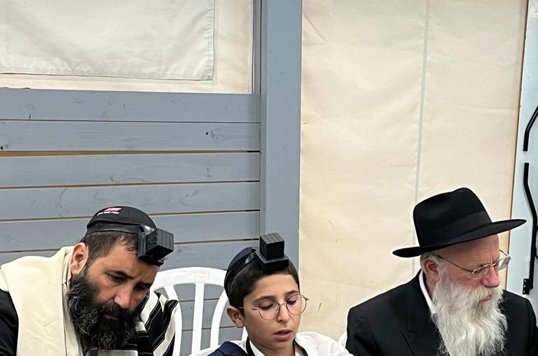 הנחת תפילין ראשונה לתמים יוני, בנו של ר' אבי מלכא, גבאי בית כנסת רייטשיק שול בכפר חב''ד
